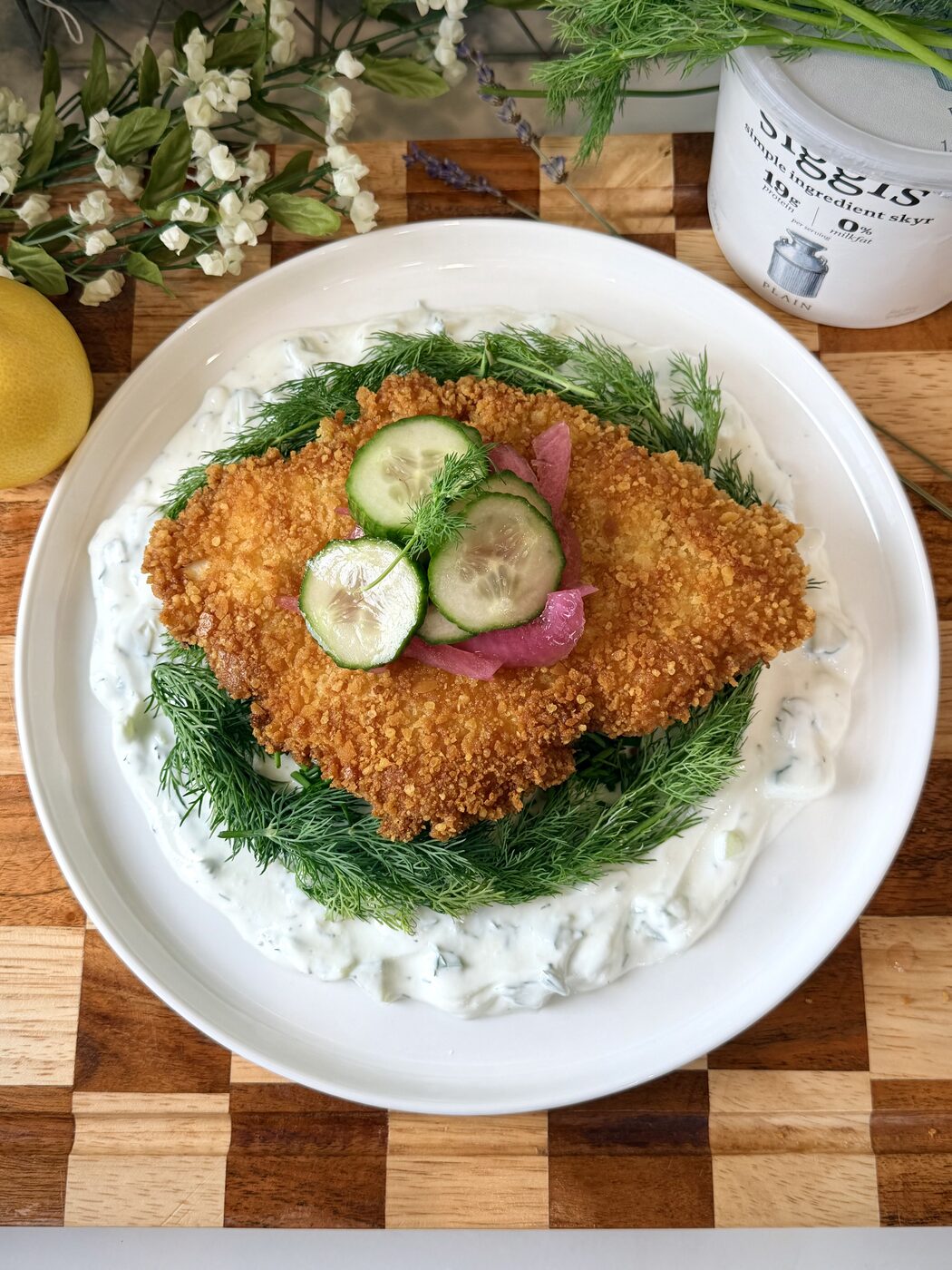 Crispy schnitzel over dill yogurt sauce with pickled onion and cucumber