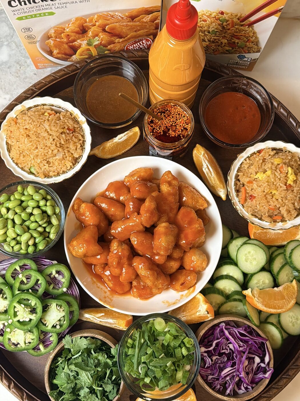 Orange chicken spread with rice, edamame and fresh vegetables on a wooden tray