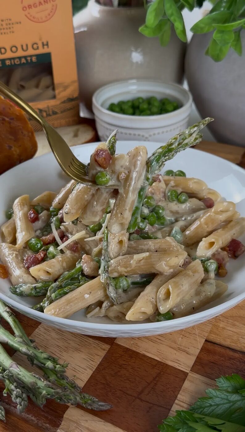Creamy penne with peas, asparagus and pancetta on a wooden board